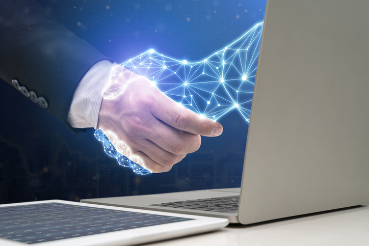 Businessman shaking hands with digital partner extending from laptop computer on futuristic background. Artificial Intelligence and Machine Learning Processes for the 4th Industrial Revolution