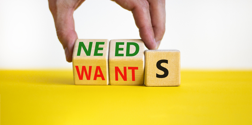 Wants or needs symbol. Businessman turns wooden cubes and changes the word wants to needs. Beautiful yellow table, white background, copy space. Business and wants or needs concept.
